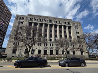 Gray court building with columns and two cars parked in front 