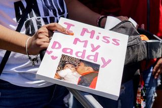 A woman holding a sign reading "I miss my daddy" with a photo of Anthony Alvarez and his baby.