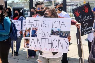 A woman holding a sign that reads "#justicia para Anthony. Killed by CPD!!!" with photos of Anthony and family.