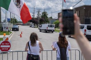 Two women in the foreground standing at a security fence, facing the Broadview facility.