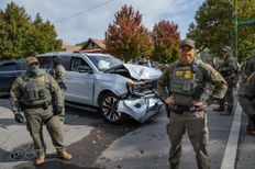 two uniformed border patrol agents standing in front of car with wrecked front en