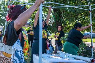 three women erecting the frame of a tent for shade