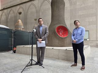 Two people standing in building atrium, one in front of mic