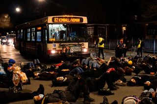 Environmental protesters lay on the road at night in front of a city bus 