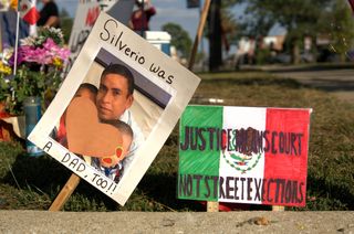 Two handmade signs sticking out of grass behind street curb. One says Silverio was a dad, too with photo of him and his children (censored). The other is Mexican flag with text overlaid JUSTICE MEANS COURT NOT STREET EXECUTIONS