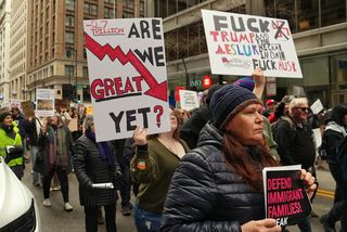 protesters marching through downtown Chicago. one is holding a sign that reads ARE WE GREAT YET?