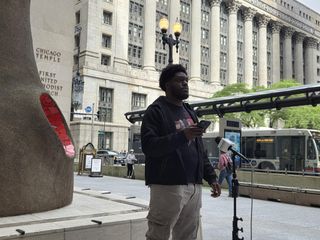 Man standing at microphone in city plaza
