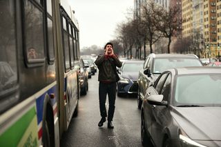 A protester in stopped traffic on lakeshore drive. They are in between lanes of cars next to a bus shouting and snowflakes are falling 