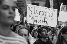 A woman holds a handmade protest sign that reads, TYRANNY OF THE MINORITY